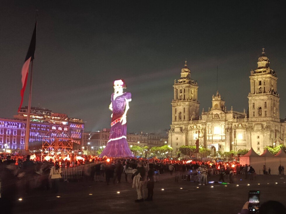 Catrina monumental de vestido morado junto a la Catedral Metropolitana en el Zócalo, iluminada de noche el 29 de octubre de 2026.